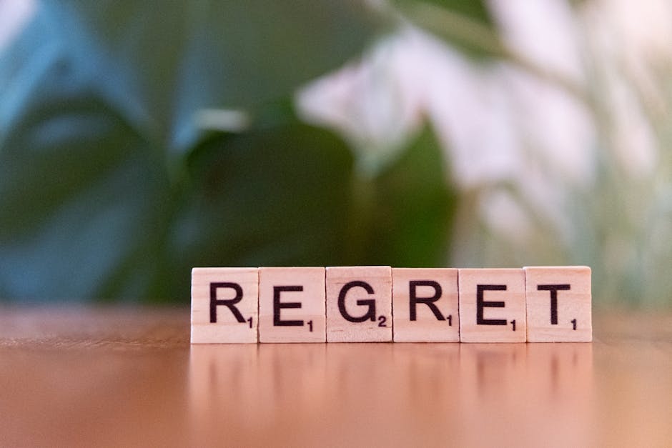 Wooden letter tiles forming the word 'Regret' on a blurred background, symbolizing emotions.